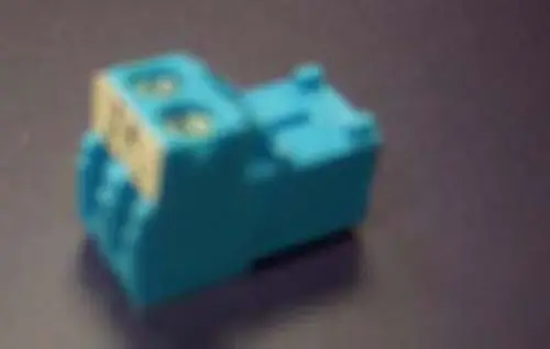Remeha Steckverbindung in blauer Farbe, mit zwei Anschlussklemmen auf der Oberseite. Abgebildet auf dunklem Untergrund, unscharf.